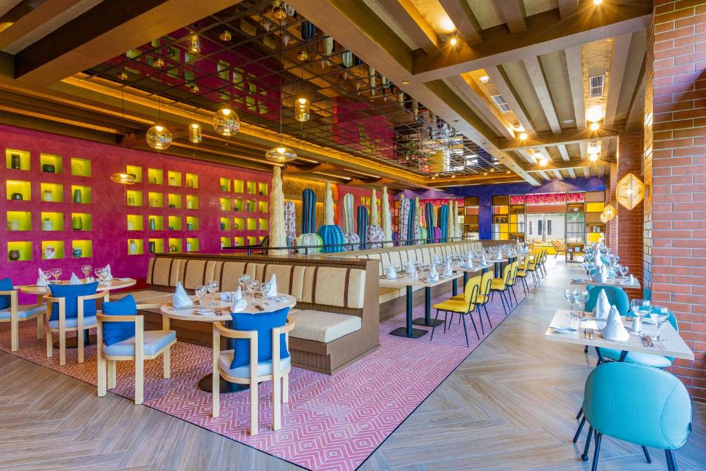 Moderns restorāns ar krāsainu interjeru, kas ietver sēdvietas ar spilgtām krāsām un dekoratīviem elementiem. Gaismas ķermeņi un spoguļi piešķir telpai mūsdienīgu atmosfēru.