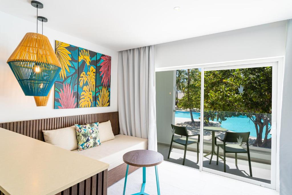 Gaiša istaba ar modernu dizainu, kurā redzama krāsaina mākslas siena un stilīgs gaismas ķermenis, kā arī skats uz peldbaseinu.