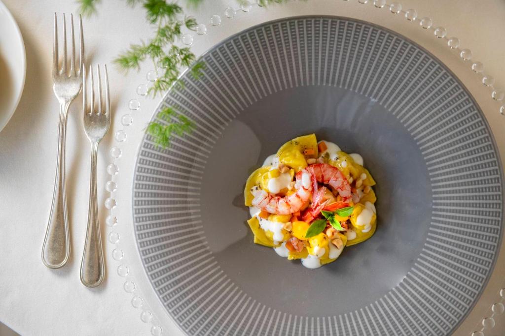 Elegants ēdiens uz pelēka šķīvja, kas satur garneles, dārzeņus un krēmīgu mērci, pasniegts ar sudraba galda piederumiem. Ideāla izvēle izsmalcinātām maltītēm.