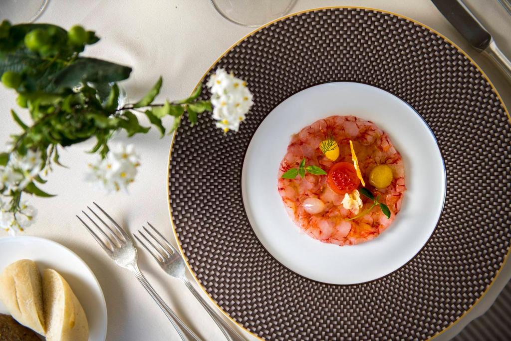 Svaiga jūras velšu uzkoda, pasniegta uz eleganta šķīvja ar dekoratīviem augļiem un garšaugiem. Uz galda redzams arī maizes gabals un ziedu kompozīcija.