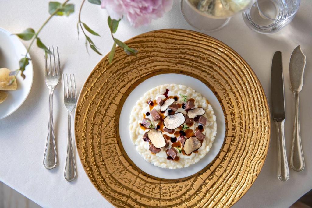 Mūsdienīgs ēdiens, kas pasniegts uz greznas zelta krāsas šķīvja, ar rīsu un sēņu kombināciju, rotāts ar zaļumiem un garšvielām. Uz galda redzami arī galda piederumi un ziedu kompozīcija.