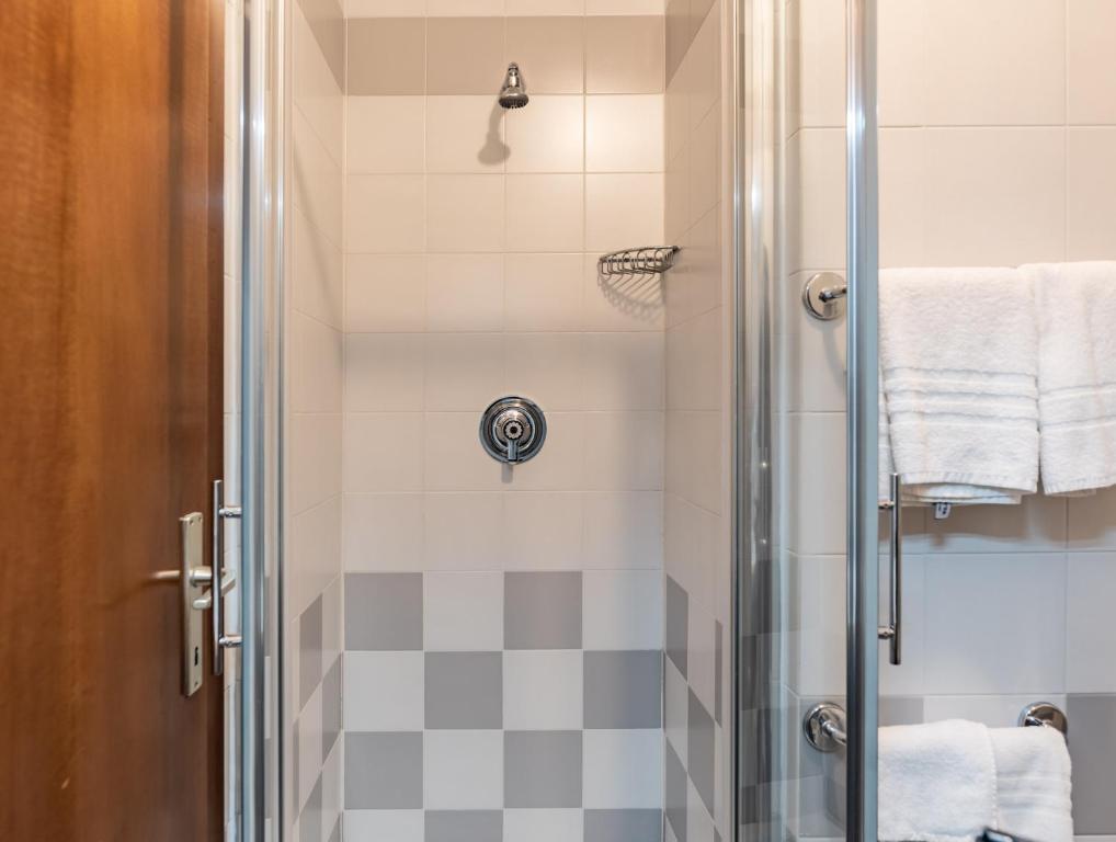 Mūsdienīga duša ar stikla durvīm un flīzēm, kas izceļ tīrību un eleganci. Dušas sienas ir gaišo toņu ar pelēkiem elementiem, radot harmonisku atmosfēru.