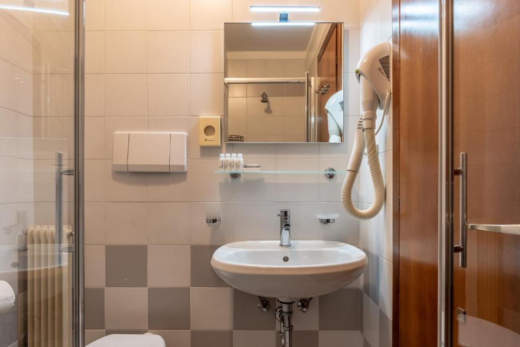 Mūsdienīgs vannas istabas interjers ar pelēku un baltu flīžu kombināciju, izlietni un spoguli, kā arī fēnu pie sienas.