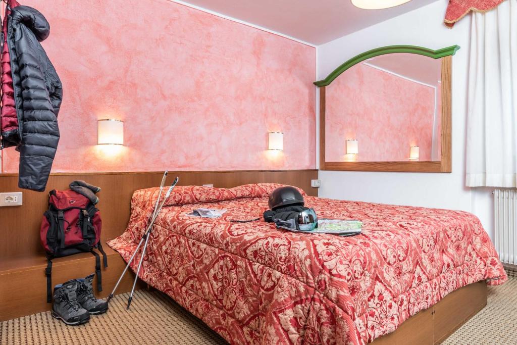Siltā un viesmīlīgā guļamistaba ar rozā sienām, dekora elementiem un gultu ar rakstainu pārklāju. Redzams mugursoma, slēpošanas zābaki un nūjas, kas norāda uz aktīvu brīvā laika pavadīšanu kalnos.