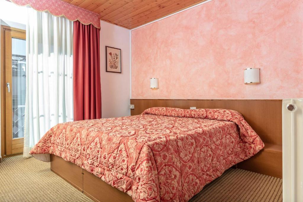 Mūsdienīga guļamistaba ar rozā sienām, sarkanu aizkaru un dīvainu gultu, kas pārklāta ar greznu palagu. Telpa ir gaiša un viesmīlīga, ar koka griestiem un logiem, kas sniedz dabīgu apgaismojumu.