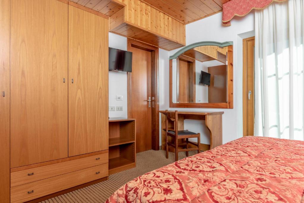 Kompakta guļamistaba ar koka mēbelēm, televizoru un rakstāmgaldu, radot mājīgu atmosfēru. Sarkanā gultas veļa piešķir telpai siltumu.