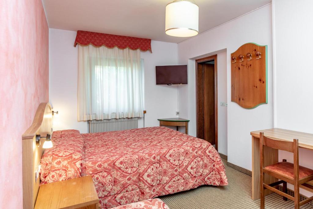 Mājas viesnīcas numurs ar divām gultām, sarkanā rakstā, koka mēbeles un televizors. Gaismas logi nodrošina dabīgu apgaismojumu.