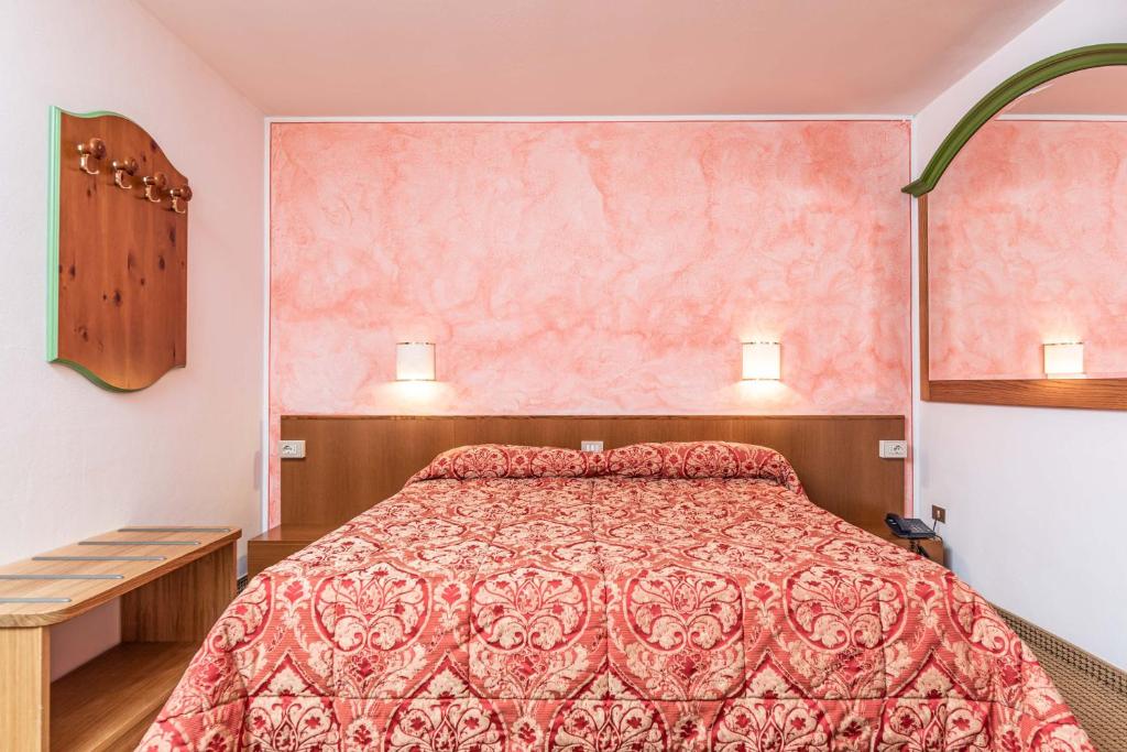 Mājīga guļamistaba ar sarkanu rakstainu gultasveļu un rozā sienām. Telpā ir koka mēbeles un apgaismojums, kas rada siltu atmosfēru.