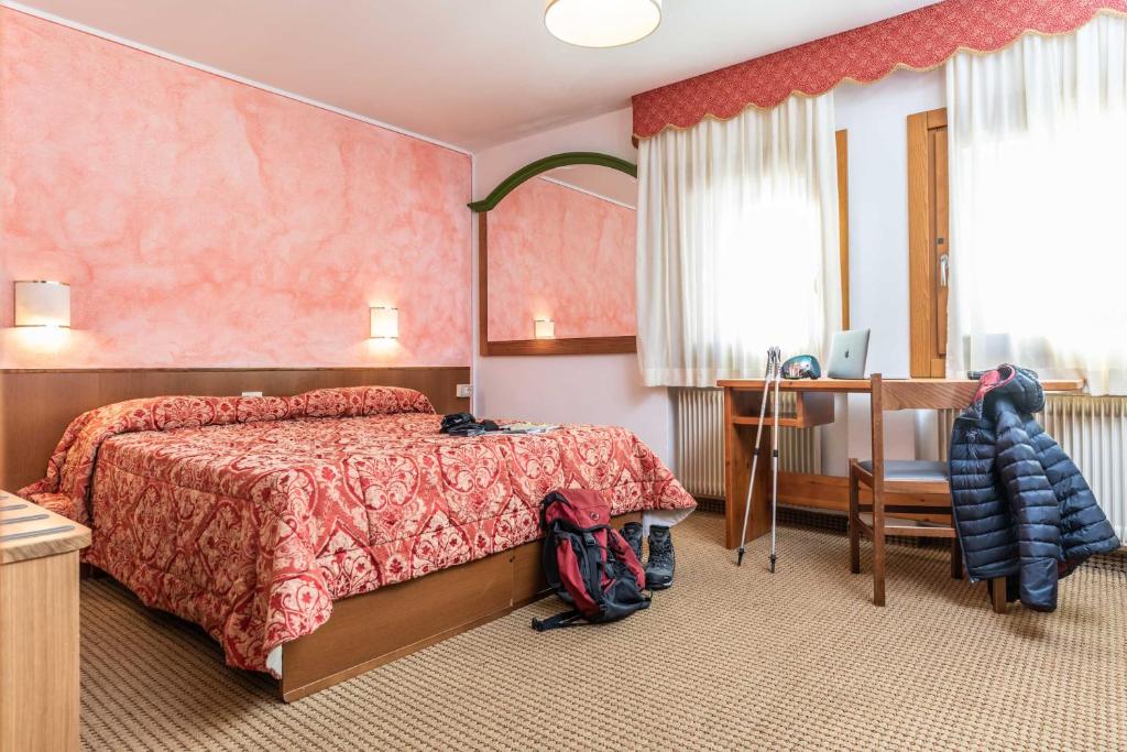 Mājīgs viesnīcas numurs ar rozā sienām, lielu gultu un rakstāmgaldu, kas aprīkots ar datoru. Numurā ir arī krēsls un bagāža, radot komfortablu atmosfēru.