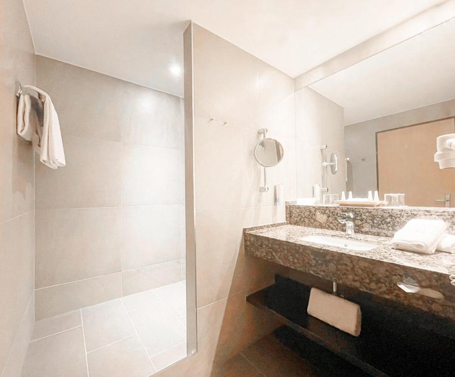 Mūsdienīgs vannas istabas interjers ar granīta izlietni, spoguli un dušu. Gaiši tonēti flīzes un minimālistisks dizains rada elegantu atmosfēru.