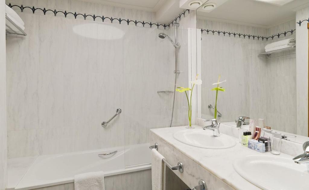 Mūsdienīgs vannas istabas interjers ar pelēku marmora apdari, divām izlietnēm un dušas zonu. Uz izlietnes novietotas kosmētikas precēm un ziedu kompozīcija.