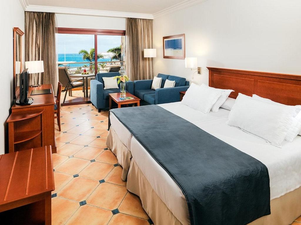 Mūsdienīga viesnīcas numura iekārtojums ar ērtu gultu, dīvāniem un skatu uz jūru. Gaismas interjers radīs patīkamu atmosfēru atpūtai.