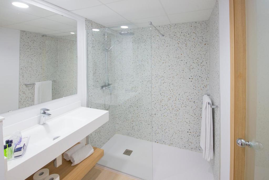 Mūsdienīgs vannas istabas interjers ar stikla dušu, gaišu izlietni un minimālistisku dizainu. Pievilcīgas akmens sienas un koka plaukts piešķir siltumu un elegance.