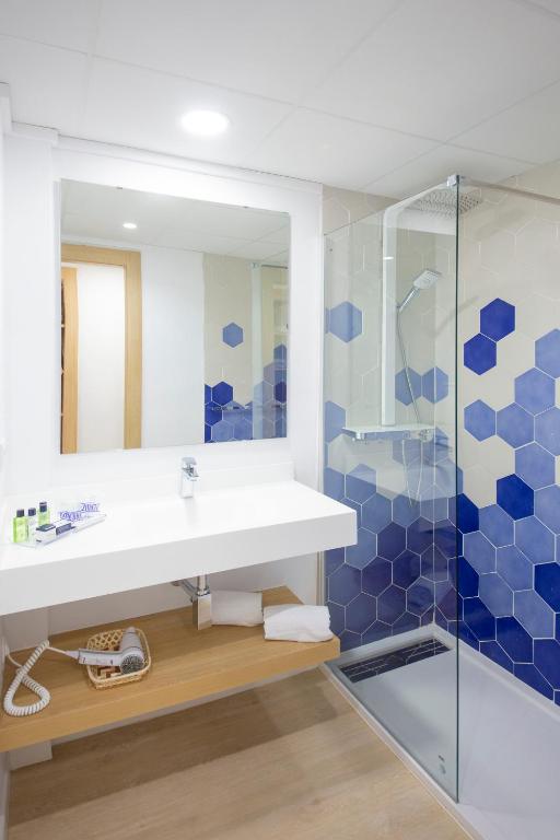 Mūsdienīgs vannas istabas interjers ar hexagonālu flīžu apdari, stikla dušu un elegantu izlietni. Vannas istabā ir pieejami higiēnas piederumi un dvieļi.