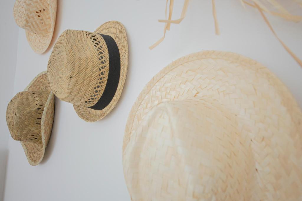 Vasaras cepures pakārtas pie sienas, izgatavotas no salmiem ar tumšu joslu. Šī fotogrāfija rada vieglu un vasarīgu noskaņu.