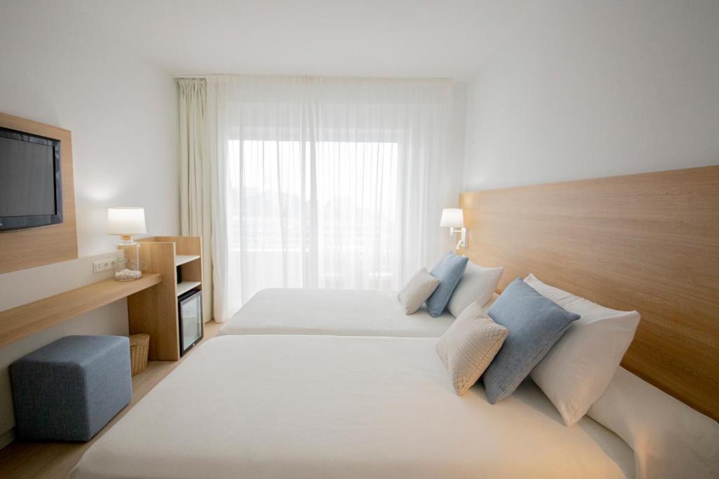 Mūsdienīga viesnīcas numura iekšskats ar divām gultām, televizoru un dabiskiem apgaismojuma avotiem. Numurā ir vienkāršs, bet elegants dizains ar viegliem toņiem un komfortablu mēbelējumu.