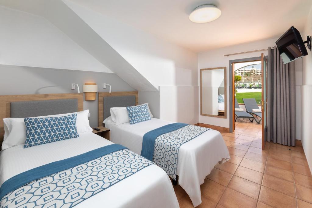 Mūsdienīga viesnīcas istaba ar divām gultām, ko rotā zila un balta dekora elementi, kā arī piekļuve terasei ar skatu uz dārzu.