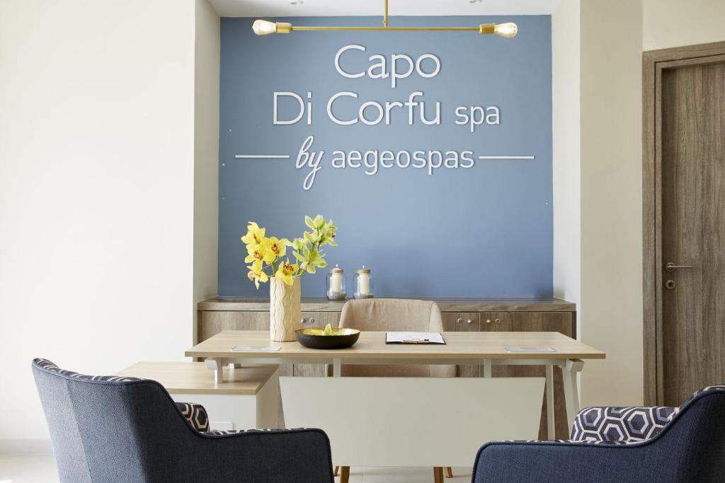 Mūsdienīgs spa interjers ar "Capo Di Corfu spa by aegeospas" logo uz sienas, dekorēts ar ziediem un elegantu mēbeļu dizainu.