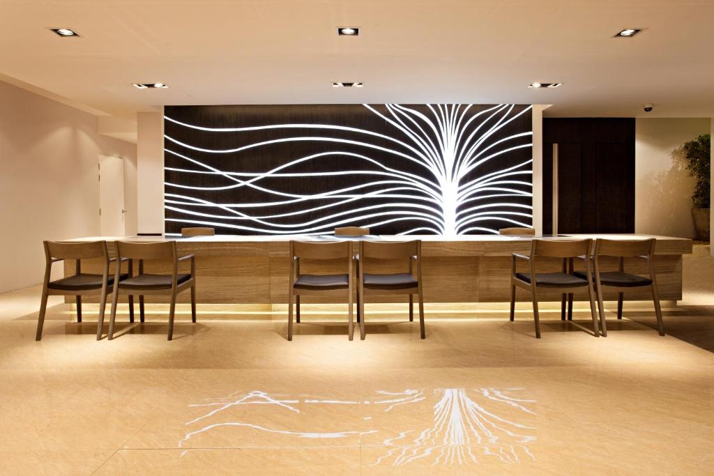 Moderns reģistratūras galds ar koka apdari un stilīgu apgaismojumu, kas atspoguļo mūsdienīgu interjera dizainu. Galds ir apvērts ar krēsliem, radot viesmīlīgu atmosfēru.