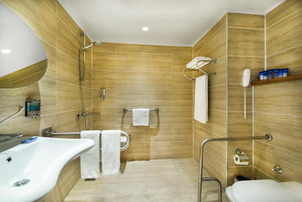 Mūsdienīgs vannas istabas interjers ar koka apdari un funkcionālu aprīkojumu, iekļaujot dušu, tualeti un izlietni. Telpa ir gaiša un plaša, nodrošinot komfortu un ērtības.