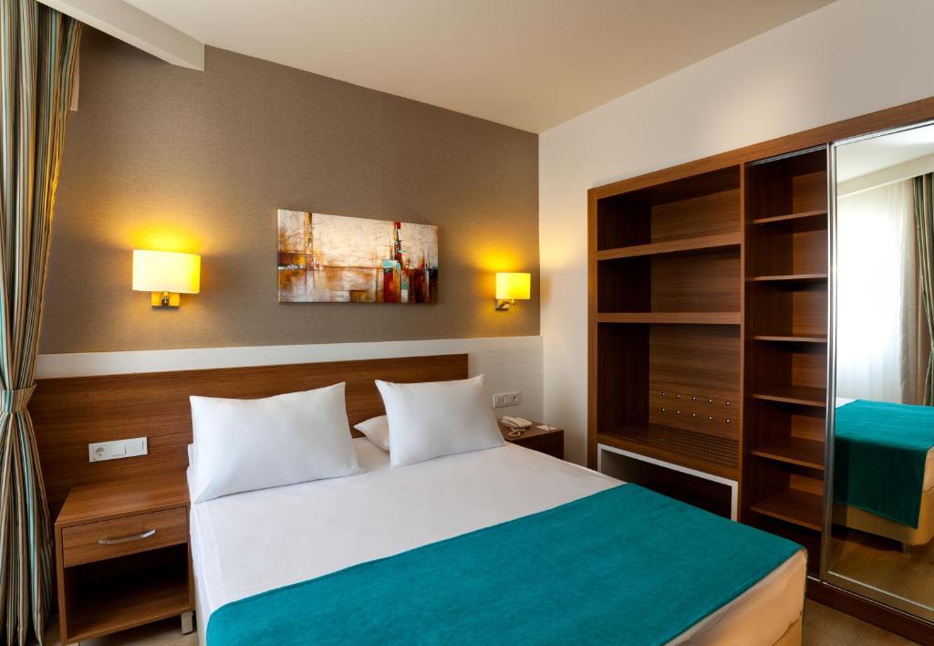 Mūsdienīga viesnīcas numura interjers ar divguļamo gultu, koka mēbelēm un gaismas elementiem. Numurā ir mākslas darbs uz sienas un atvērtas plauktu sistēmas.