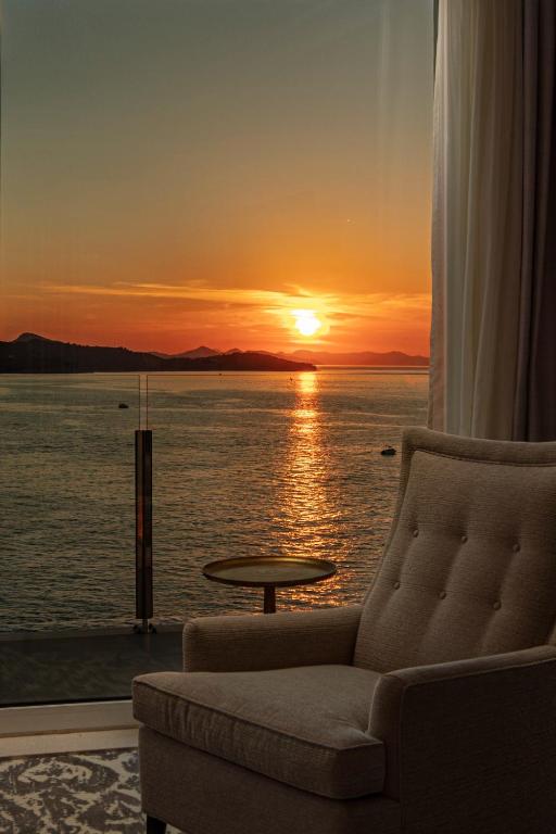 Saulriets virs ūdens ar kalniem fona, redzams no mājīgas krēsla. Šis skats rada mierīgu un relaksējošu atmosfēru.