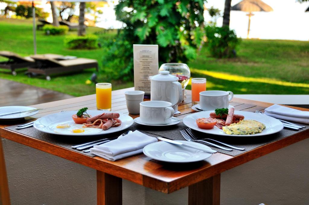 Broka bakstāmas klātas galds ar dažādām brokastu ēdienu iespējām, tostarp omleti, desiņām un olu, kopā ar dzērienu un tējas servisu, ar zaļo dabu fona.