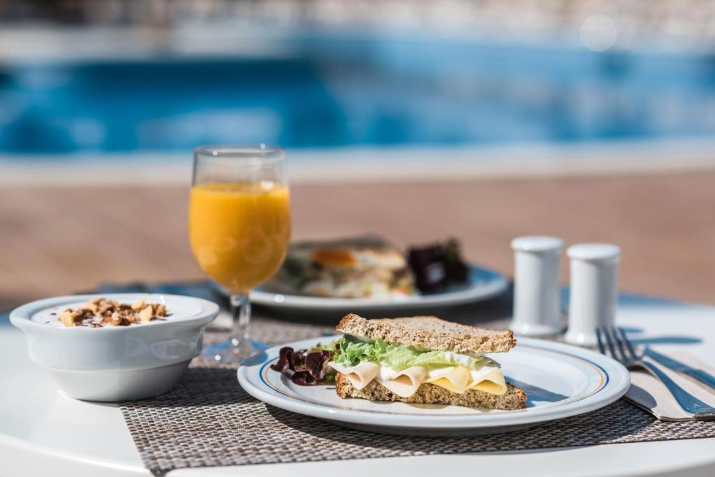 Broša ar sieru un salātiem, jogurts ar granola un apelsīnu sula, pasniegta pie baseina.