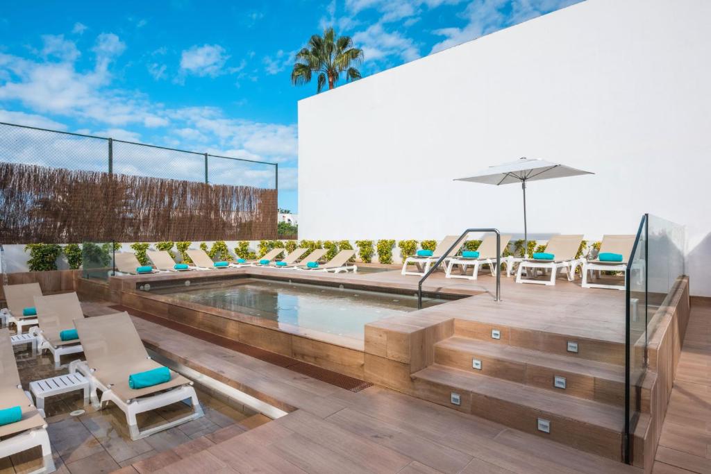 Mūsdienīgs baseins ar saules krēsliem un sauļošanās vietu, apstādījumi un debesis ar mākoņiem.