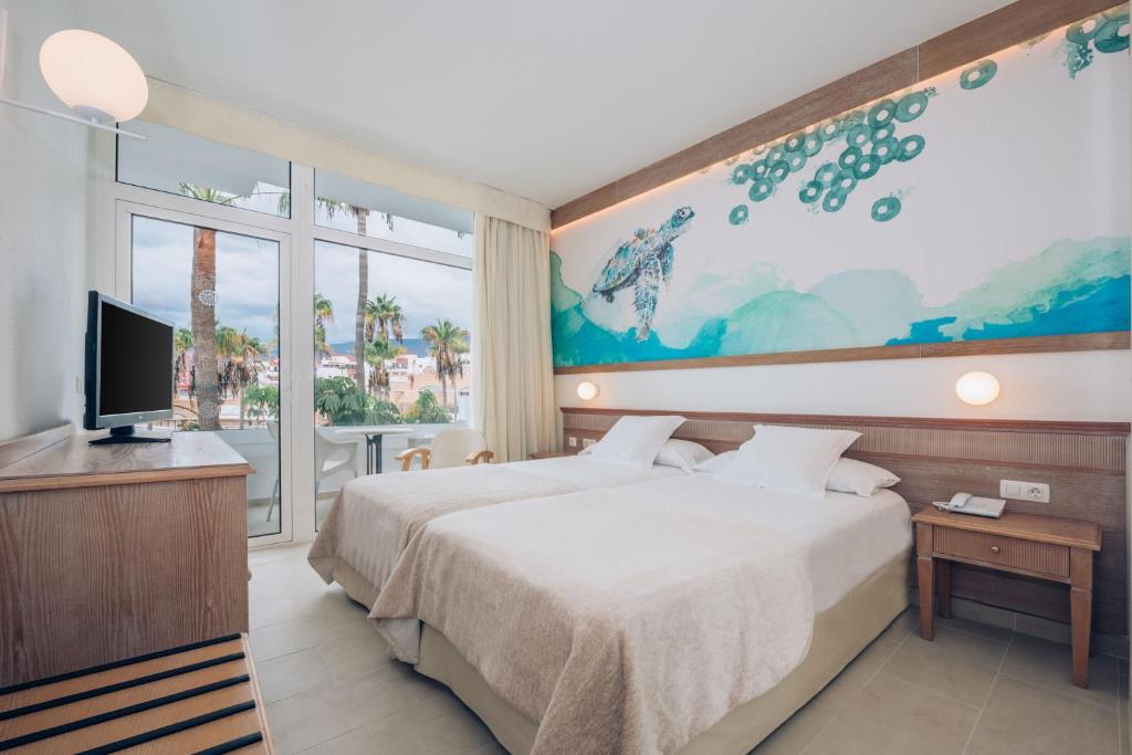 Mūsdienīgs viesnīcas numurs ar divām gultām, koka mēbelēm un jūras tēmu sienas gleznojumu. No logiem paveras skats uz palmām un ārējo terasi.