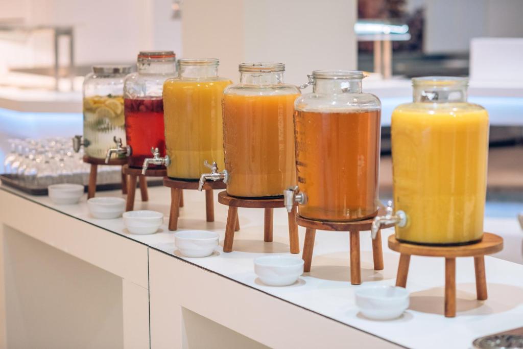 Dzērienu stacija ar vairākām stikla kannām, kas satur dažādus dzērienus, piemēram, limonādi un sulu. Katrs dzēriens pasniegts uz koka statīva, blakus maziem traukiem.