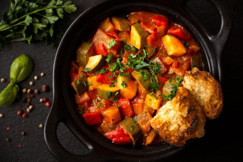 Svaiga dārzeņu sautējuma porcija ar zaļumiem un grauzdētu maizi. Ideāli piemērots veselīgai maltītei.