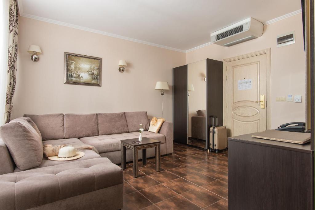 Mūsdienīga viesnīcas numura iekšskats ar ērtu dīvānu, kafijas galdiņu un lielu spoguli. Telpa ir gaiša un viesmīlīga, ar elegantiem apgaismojuma elementiem un dekoratīvām gleznām uz sienām.