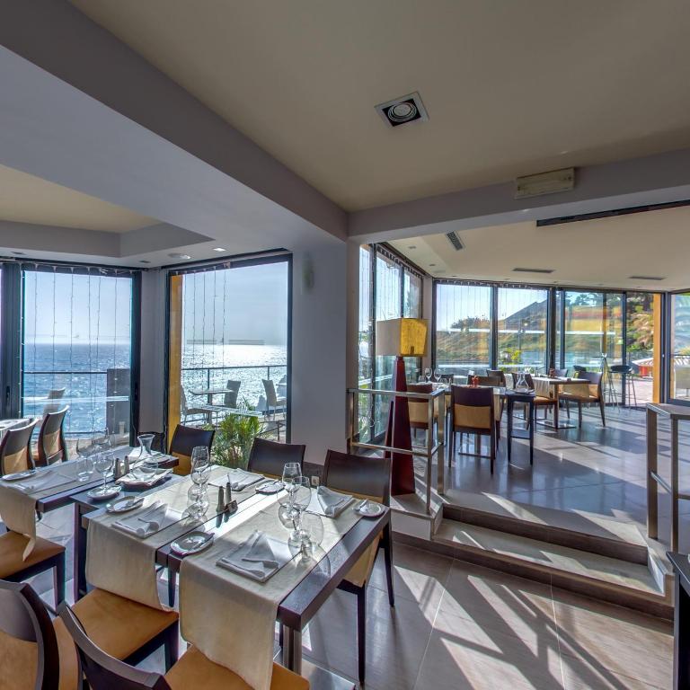 Mūsdienīgs restorāns ar jūras skatu, kurā ir elegantas galda klājumi un plašas logu sienas, kas nodrošina dabīgu apgaismojumu. Ideāla atmosfēra relaksējošām maltītēm.