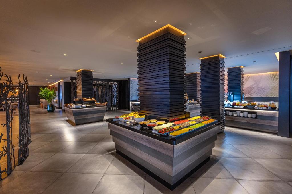 Mūsdienīga restorāna iekārtojums ar bufeti, kurā redzami krāsaini dārzeņi un augļi, kā arī eleganti galdi un apgaismojums. Interjers izceļas ar modernām līnijām un neparastu dizainu.