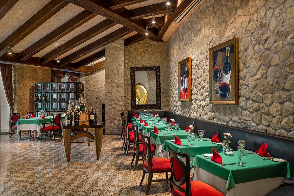Elegantā restorāna interjers ar akmens sienām, koka sijām un zaļiem galdiem, rotātiem ar sarkaniem salvetēm. Dekorēts ar mākslas darbiem, kas attēlo vīnus un šampanieti.