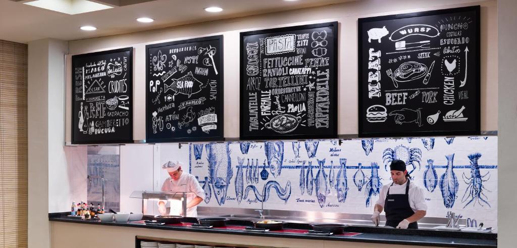 Kulinārijas virtuve ar šefpavāru, kas gatavo ēdienus, un melnā krāsā rakstītu ēdienu izvēlni uz sienas.