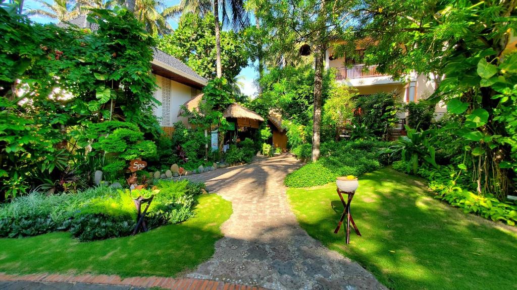 Skaista dārza ainava ar zaļajiem augiem, akmeņiem un ceļu, kas ved uz spa ēku, ko ieskauj tropu veģetācija.