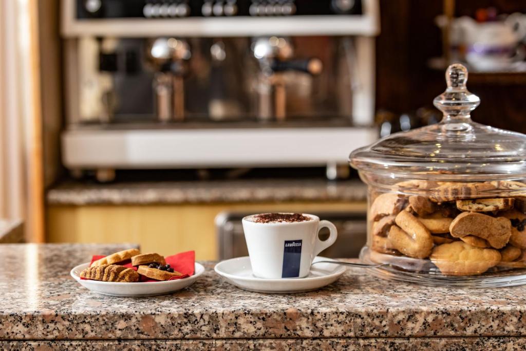 Kafijas tase ar cepumiem uz galda, blakus stikla traukā ar dažādiem cepumiem. Ideāla uzkodu un kafijas kombinācija.