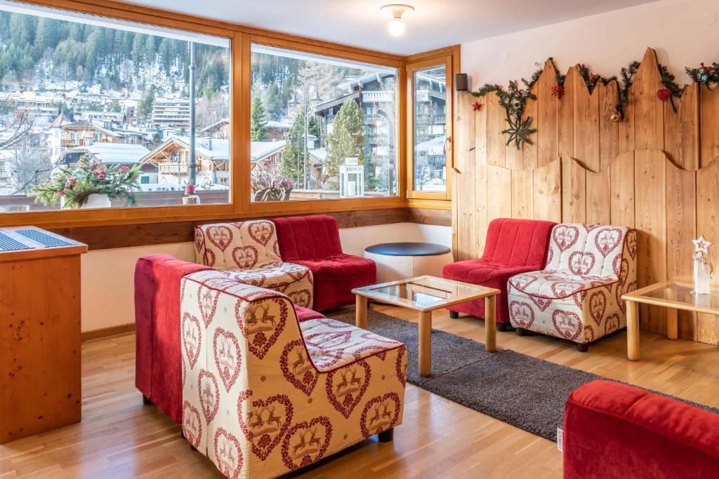 Mūsdienīga viesnīcas viesistaba ar sarkaniem dīvāniem un koka sienu, kas dekorēta ar Ziemassvētku rotājumiem. Logi piedāvā skatu uz kalniem un apkārtējo dabu.