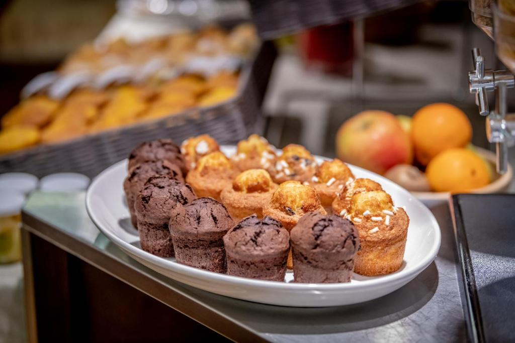 Saldumu plate ar šokolādes un vaniļas cepumiem, ieskaitot augļu grozu ar āboliem un apelsīniem fonā.