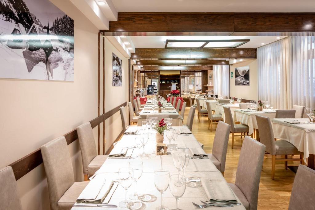 Mūsdienīgs restorāns ar elegantiem galdiem un krēslām, kas gaida viesus. Interjers ietver koka elementus un mākslas darbus, radot patīkamu atmosfēru.