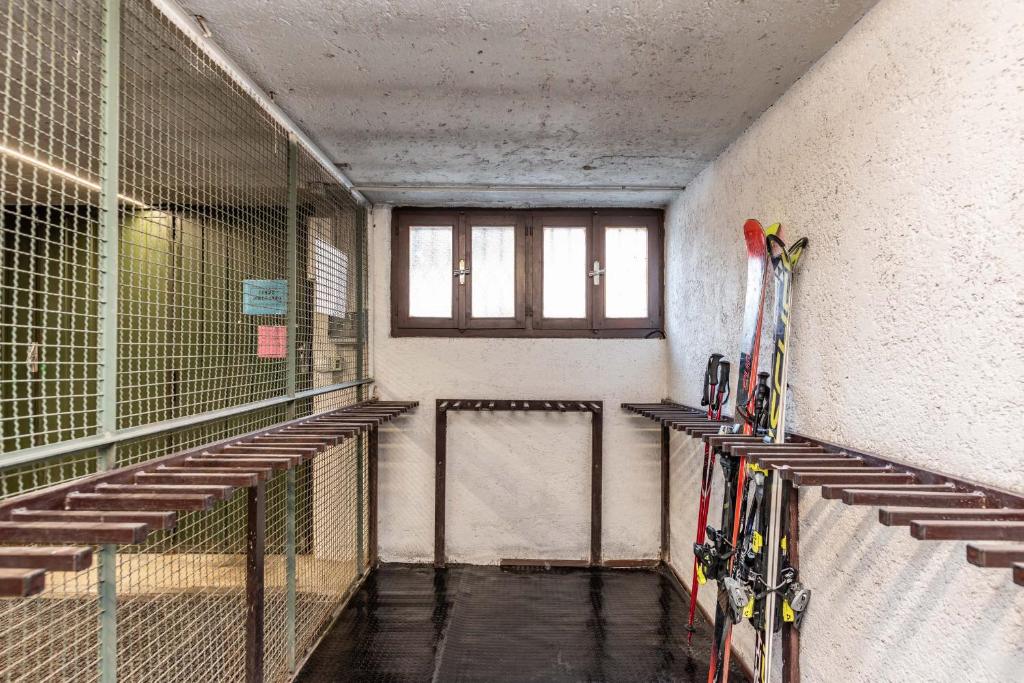 Slēpošanas equipment uzglabāšanas telpa ar koka plauktiem un logiem. Telpas iekārtojums ir vienkāršs un funkcionāls, piemērots slēpju novietošanai.