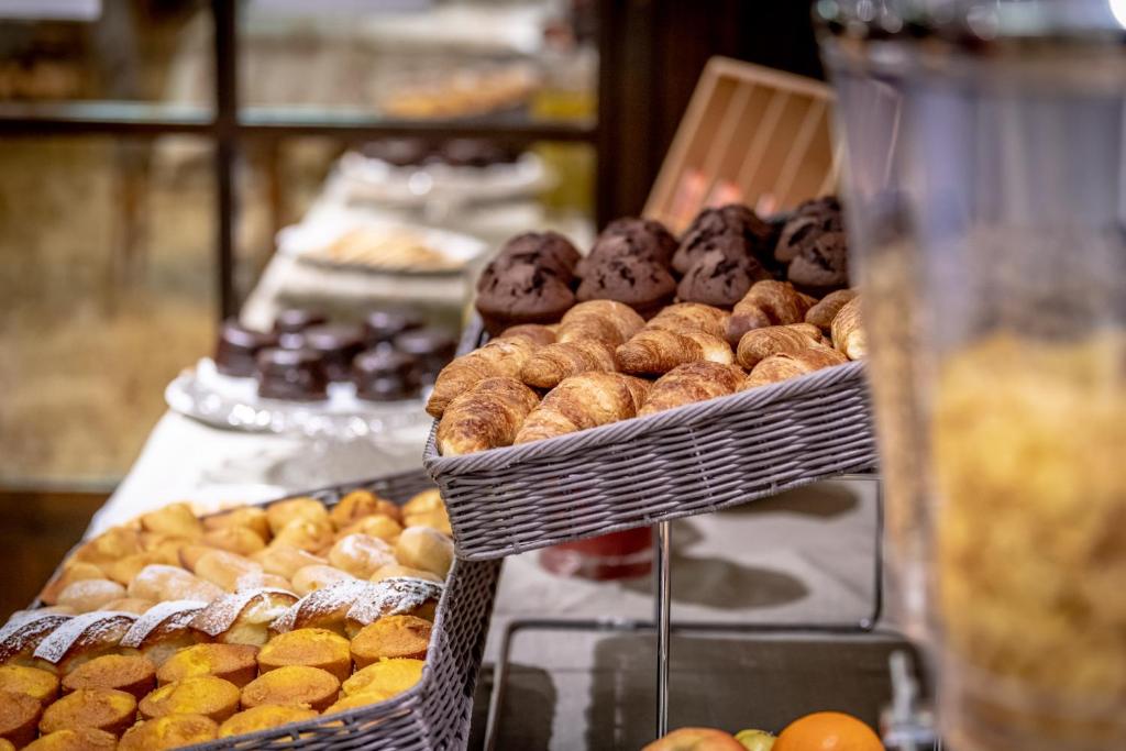 Maizes izstrādājumu stends ar dažādiem gardumiem, tostarp kruasāniem un saldām maizītēm, kas sakārtotas ratiņos. Fons papildina desertu un augļu izvēli.