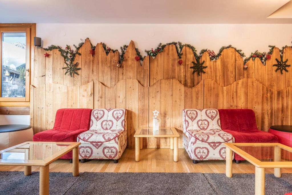 Mūsdienīgs interjers ar koka sienu un dekoratīvām rotājumiem, diviem komfortabliem dīvāniem un stikla galdiem. Telpa ir gaiša un siltā atmosfērā, ideāli piemērota atpūtai.