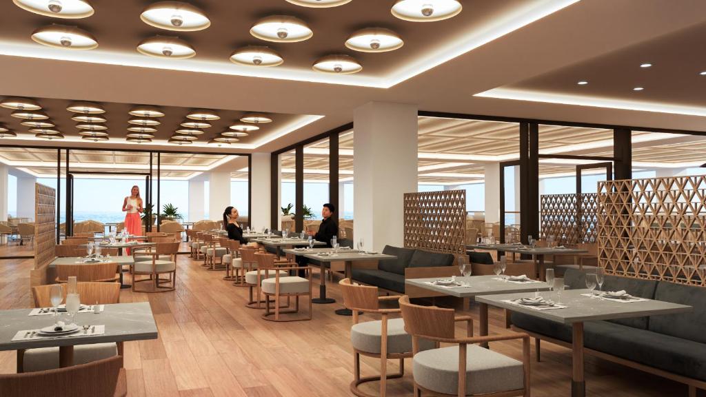Moderns restorāns ar elegantu interjeru, kurā redzami viesi, kas bauda maltītes. Gaismas un koka elementi rada siltu atmosfēru.