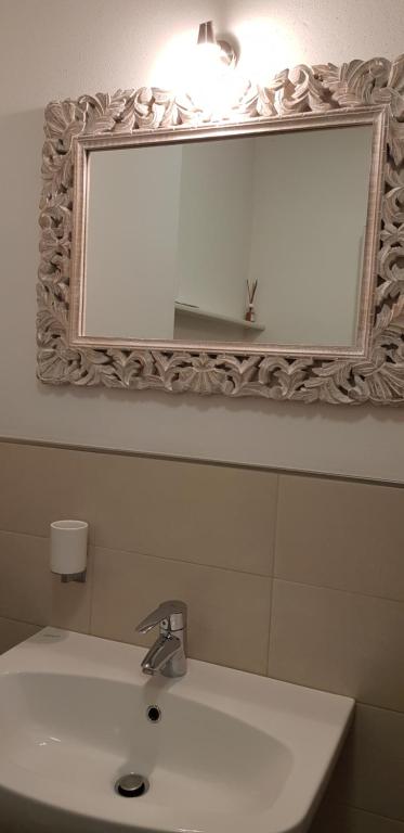 Eleganta vannas istabas spogulis ar izsmalcinātu rāmji, kas rotāts ar augu motīviem, apgaismots ar modernu lampu. Blakus atrodas mūsdienīga izlietne ar hromētu jaucējkrānu.