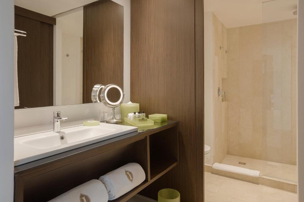 Mūsdienīgs vannas istabas interjers ar koka akcentiem, izsmalcinātu izskatu un modernām higiēnas precēm. Apgaismojums un spogulis papildina telpas eleganci.