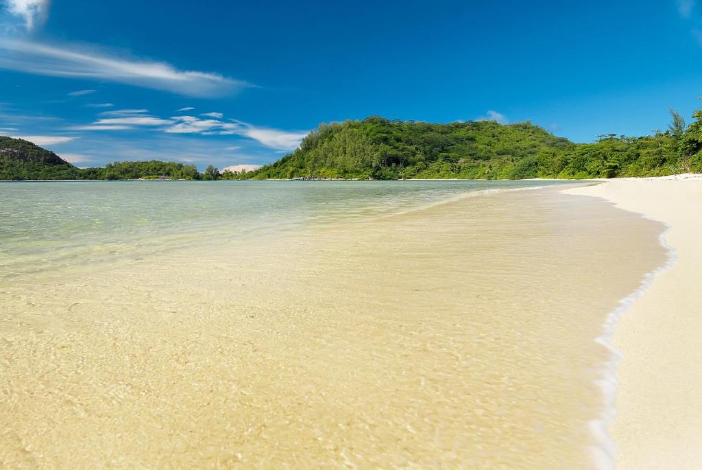 Skaisti pludmales skati ar baltu smiltīm un mierīgu ūdeni, ko ieskauj zaļš kalns un skaidras debesis. Ideāla vieta atpūtai un relaksācijai.