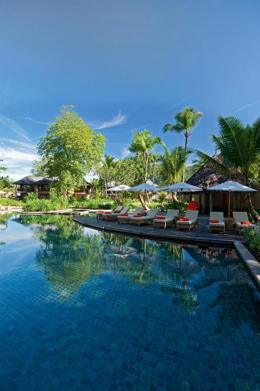 Viesmīlības vietas piebaseins ar sauļošanās krēsliem un palmu kokiem, kas rada tropisku atmosfēru. Gleznainais skats uz zilo debesi un zaļajām ainavām nodrošina mierīgu un relaksējošu vidi.